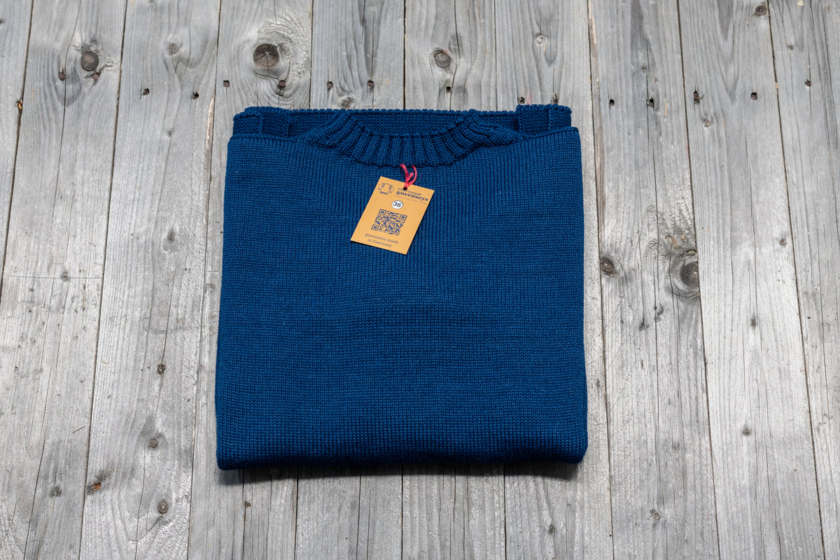 Folded GG Blue traditional wool guernsey sweater with a size 36 tag on a rustic wooden background.