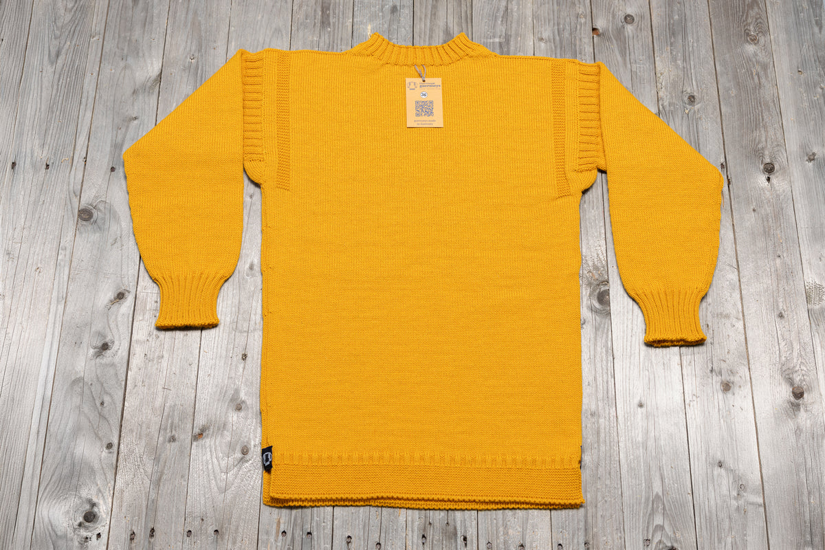 Traditional yellow wool guernsey sweater with ribbed cuffs and shoulders, laid flat on a rustic wooden background.