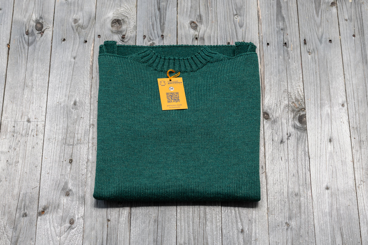 Folded Salty Sea green traditional wool guernsey sweater with size 36 tag on a rustic wooden background.
