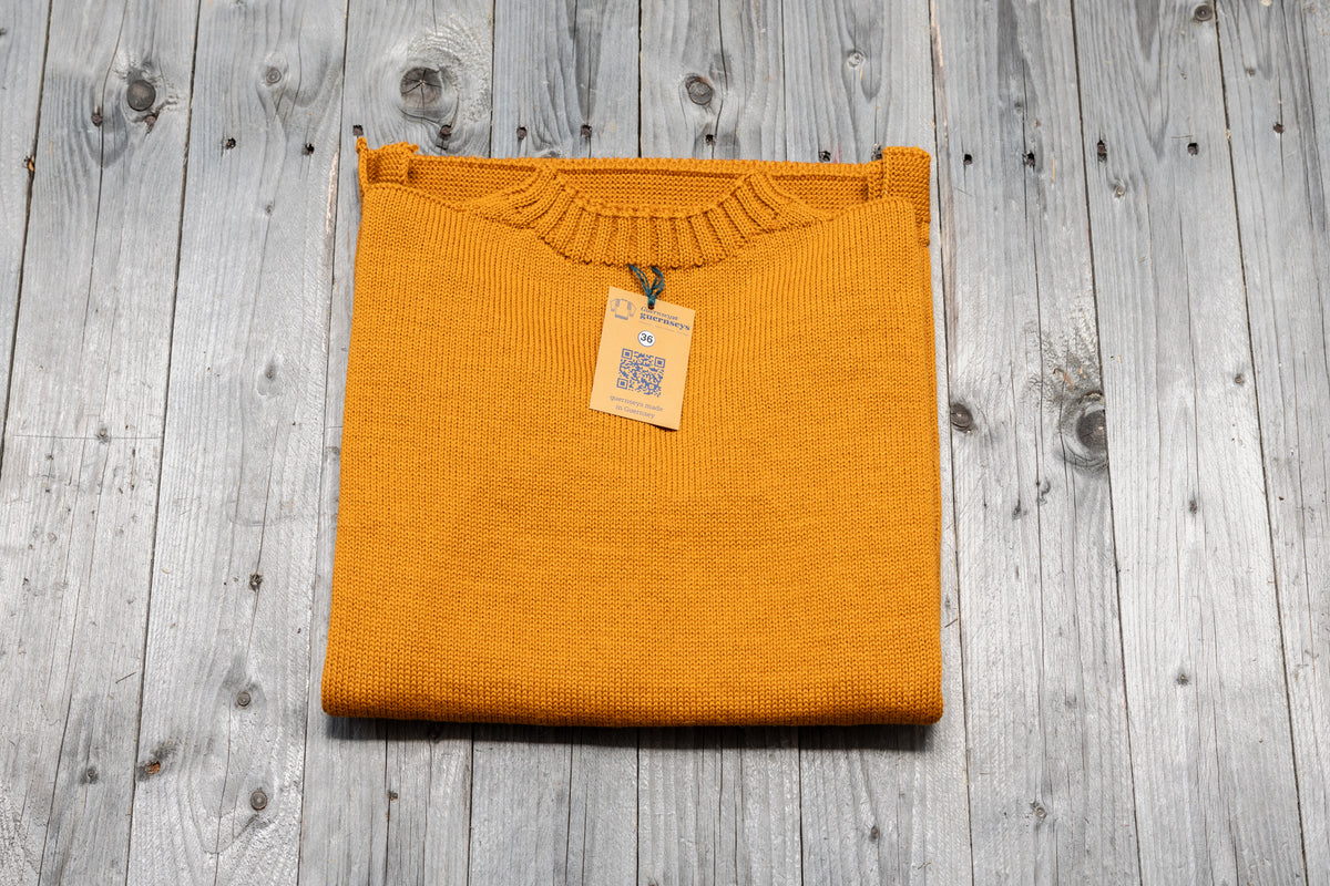 Golden yellow pure wool traditional guernsey sweater with size 36 tag, folded on a rustic wooden surface.