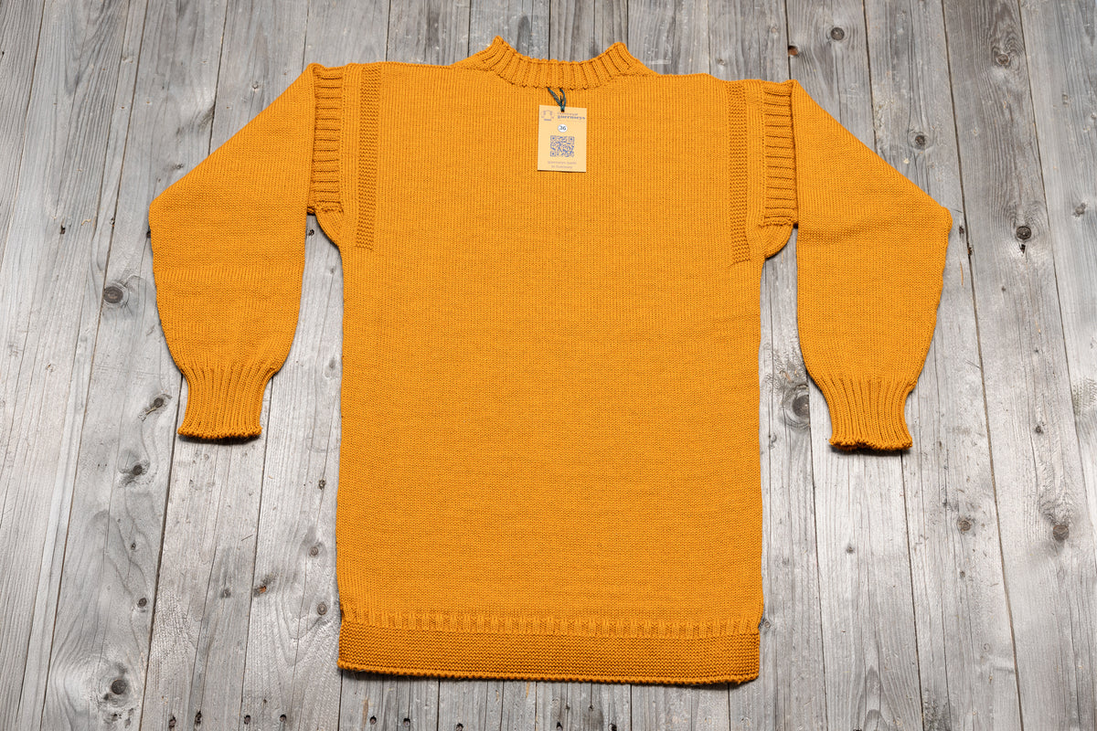 Golden yellow traditional pure wool guernsey sweater with ribbed cuffs and shoulder detailing on a wooden background.