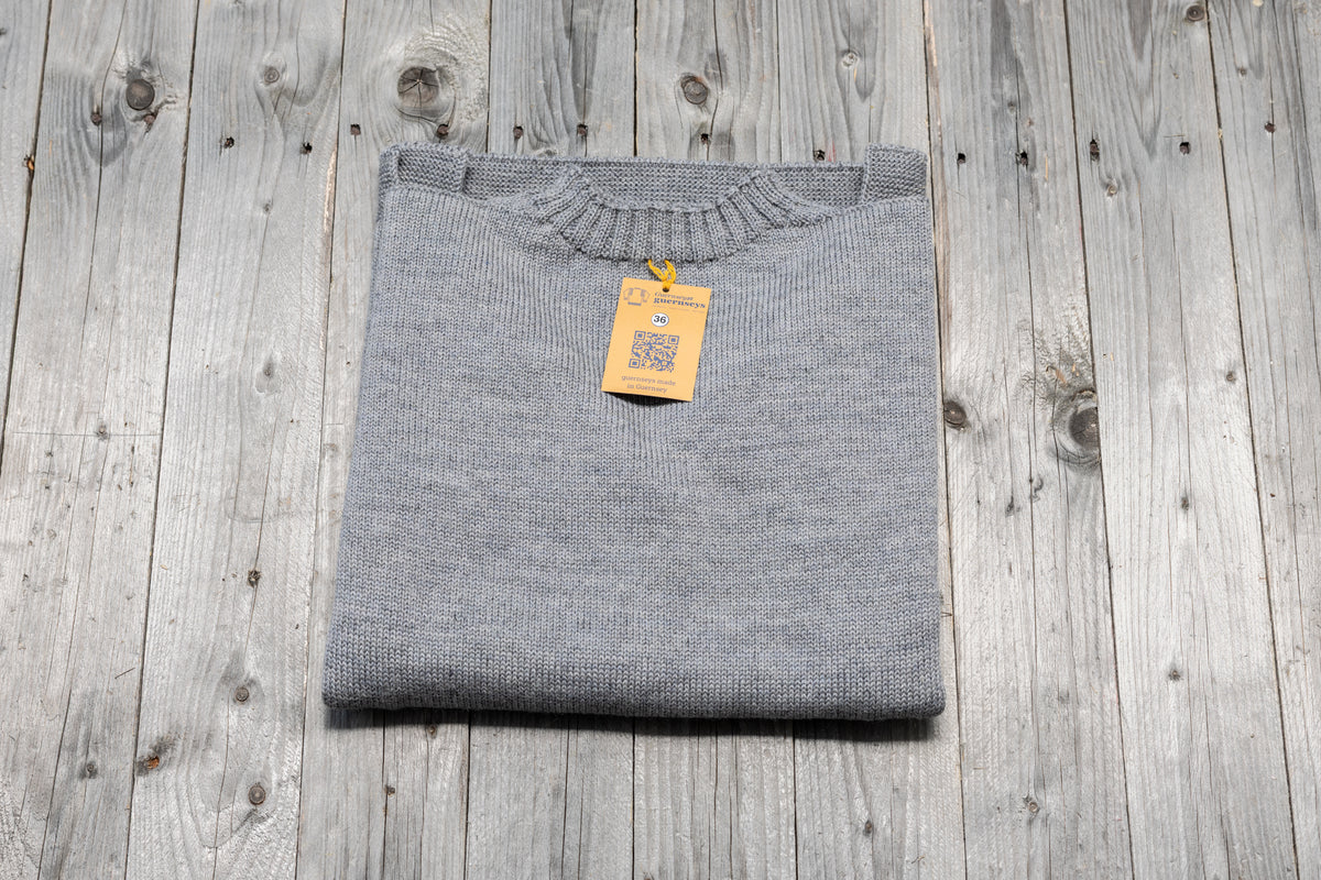 Folded granite grey traditional wool guernsey sweater with a size 36 tag on a rustic wooden background.