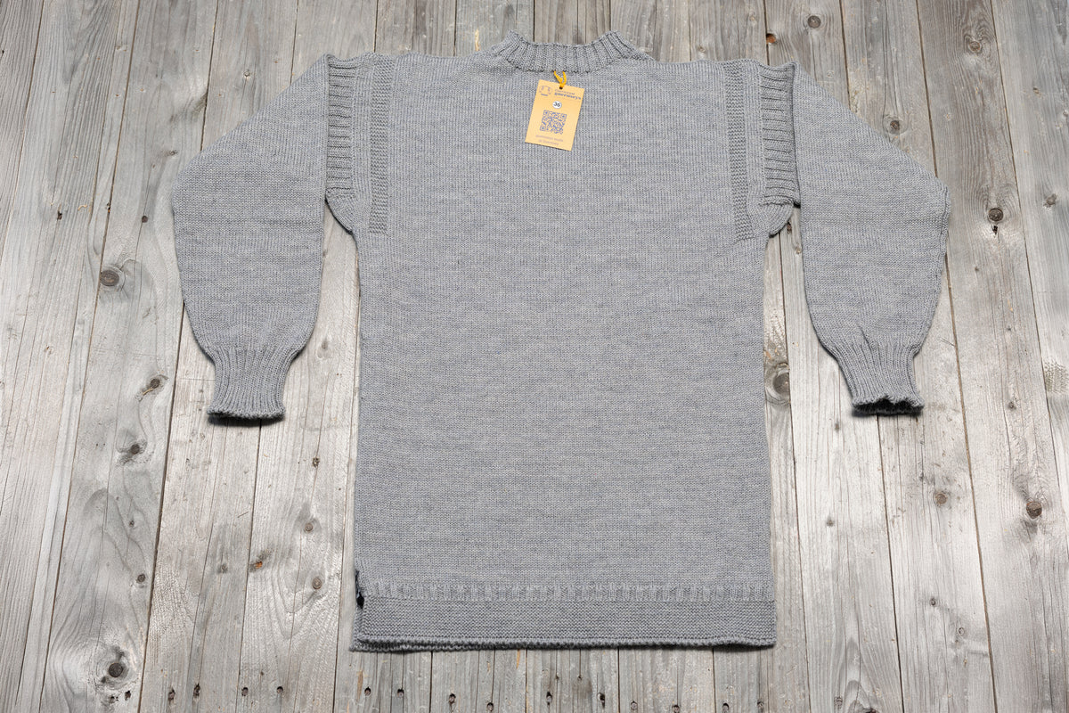 Traditional granite grey wool guernsey sweater with ribbed cuffs and collar on a rustic wooden background.