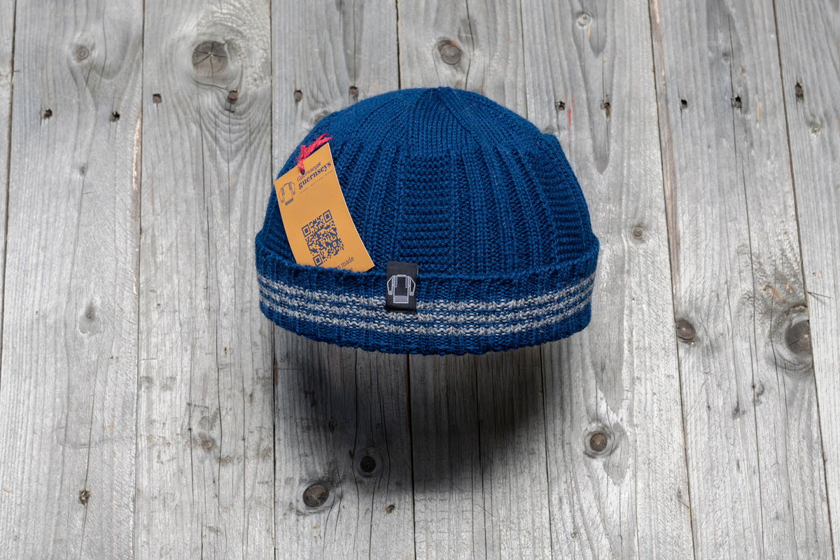 Blue wool Hanois beanie with a ribbed knit design, reflective turn-back cuff, and brand tag on a rustic wooden background.