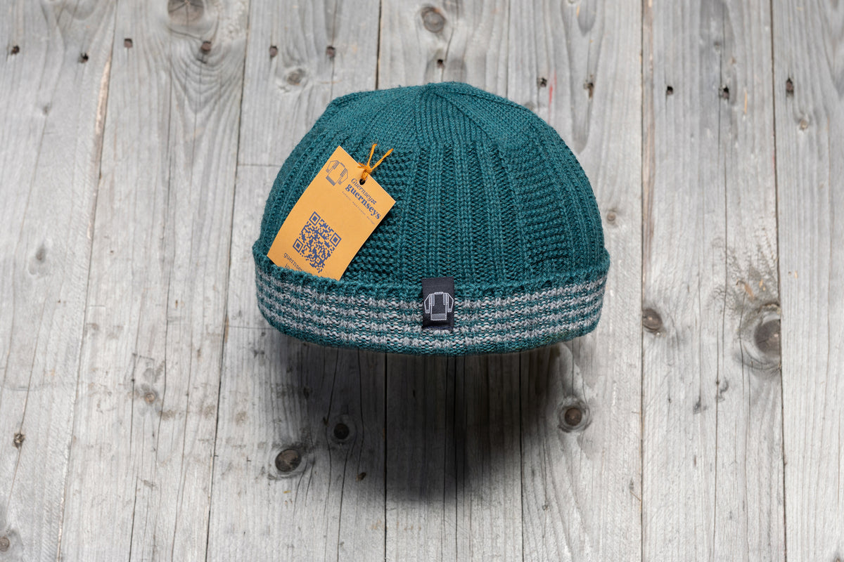 Teal wool Hanois beanie with a ribbed knit, turn-back cuff, and reflective grey bands on a rustic wooden background.