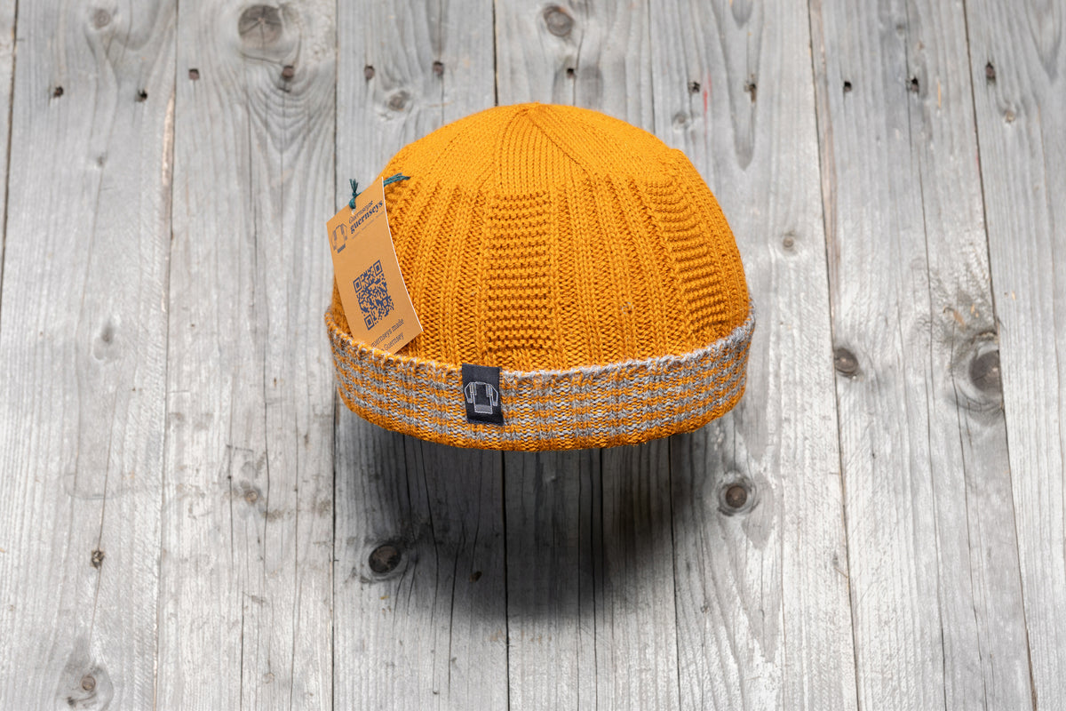 Mustard yellow wool Hanois beanie with a reflective turn-back cuff and branded tag on a rustic wooden background.