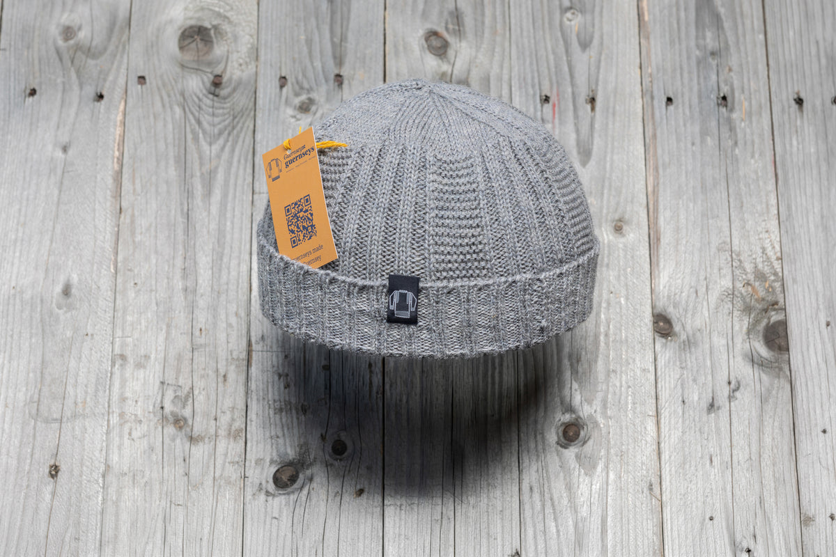 Grey wool Hanois beanie with a ribbed knit design, turn-back cuff, and branded tag on a rustic wooden background.