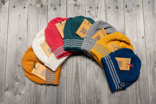 A collection of colorful, pure wool Hanois beanies with reflective striped turn-back cuffs, arranged on a wooden surface.